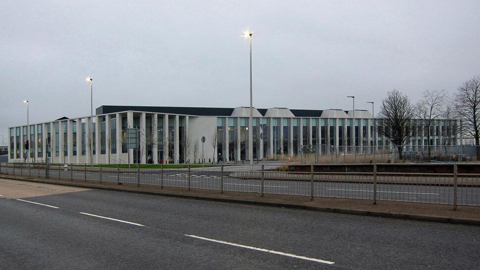 The court building has a series of pillars along its exterior walls. The road normally busy road outside is quite. There are three streetlights switched on.