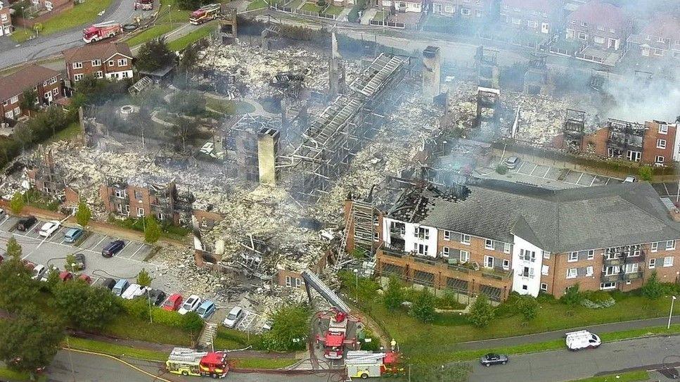 An aerial view showing a building which has been devastated by fire with fire engines in the foreground and background