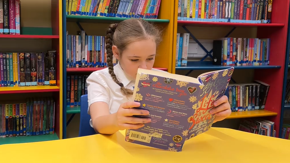 Harper reading a book on a yellow table at her school library