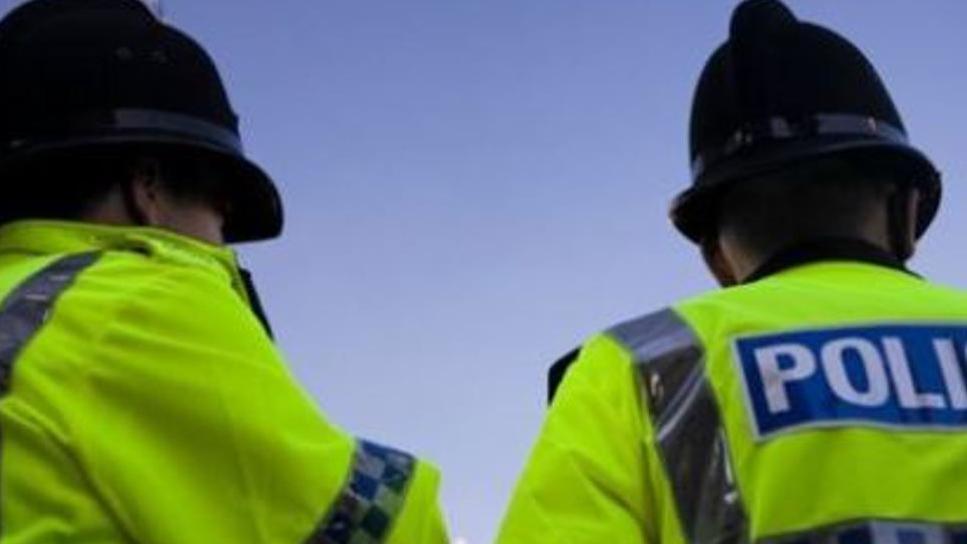 A close-up of two police officers wearing yellow high-visibility jackets and black helmets