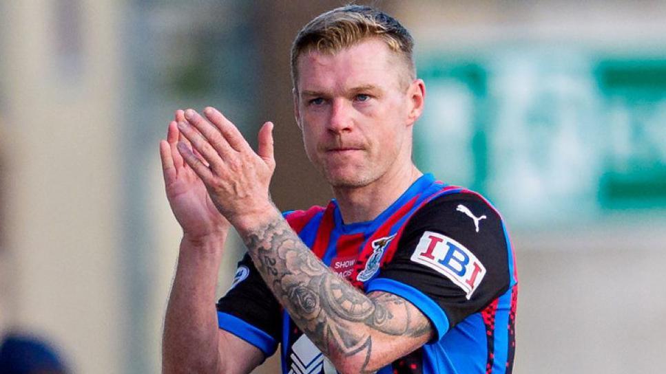 Billy Mckay claps his hands. He is wearing Inverness' home kit and has a tattoo on his left arm.