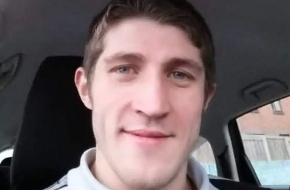 Allan Marshall smiling at the camera. he is in a car and is wearing a light-coloured polo shirt. He has dark hair.