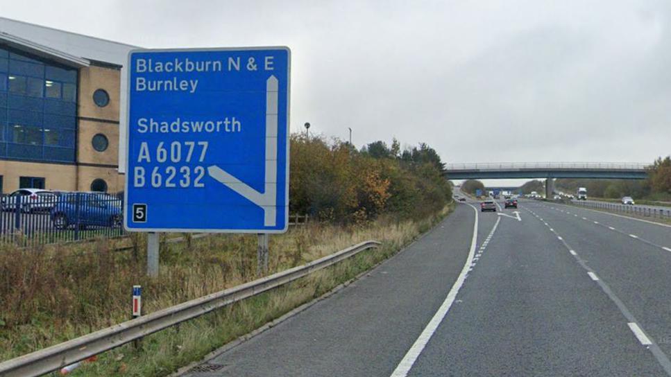 A blue motorway sign for junction 5 of the M65, pointing straight head to Blackburn and Burnley and to the left for Shadsworth