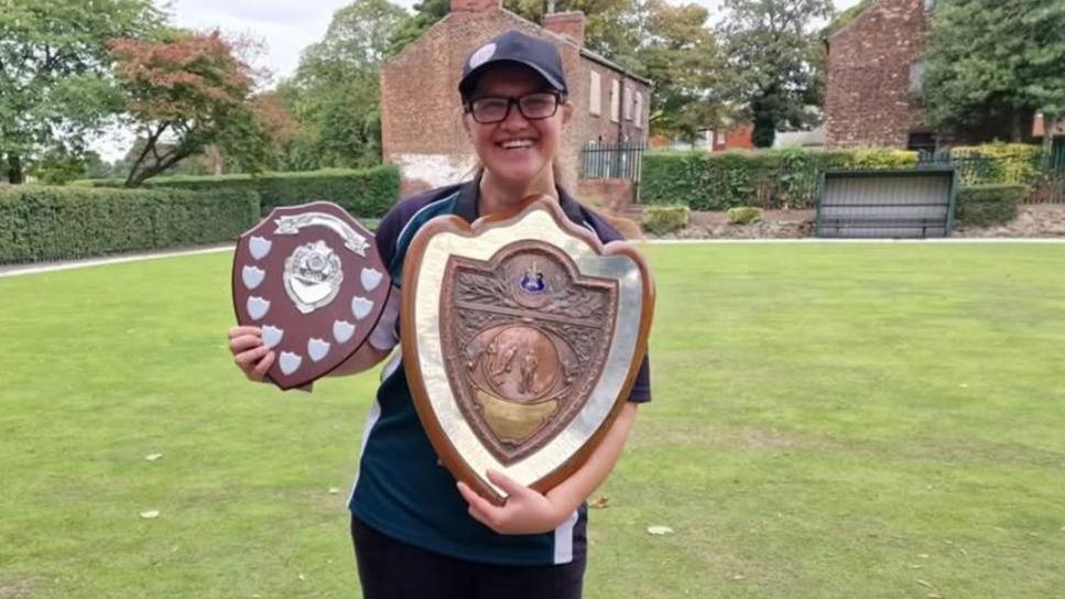 Laura Fulleylove holding her award shields while standing on a bowling green