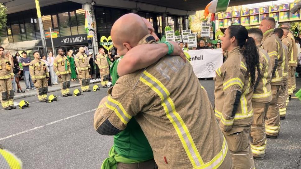 Firefighters stand either side of a street as Grenfell tower marchers go by