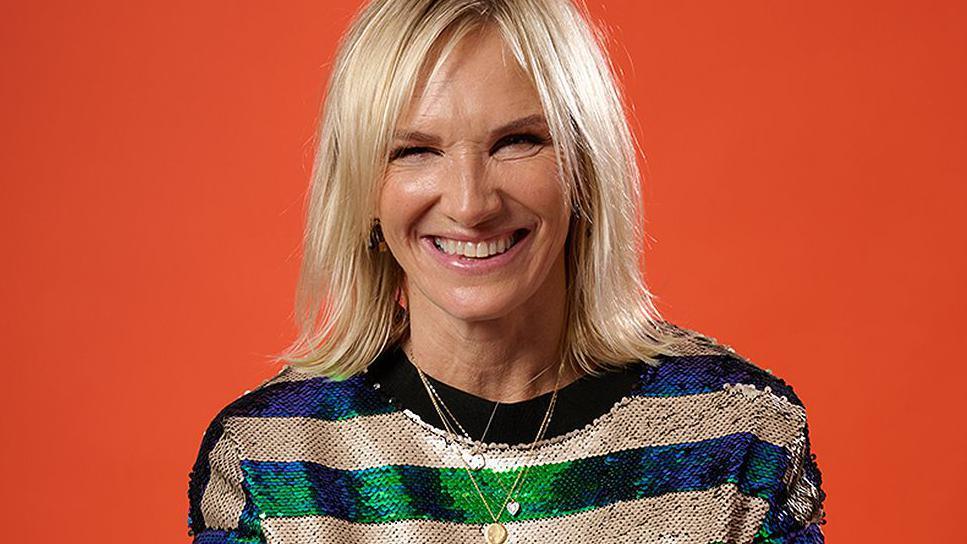 Jo Whiley smiling broadly in front of a bright orange background