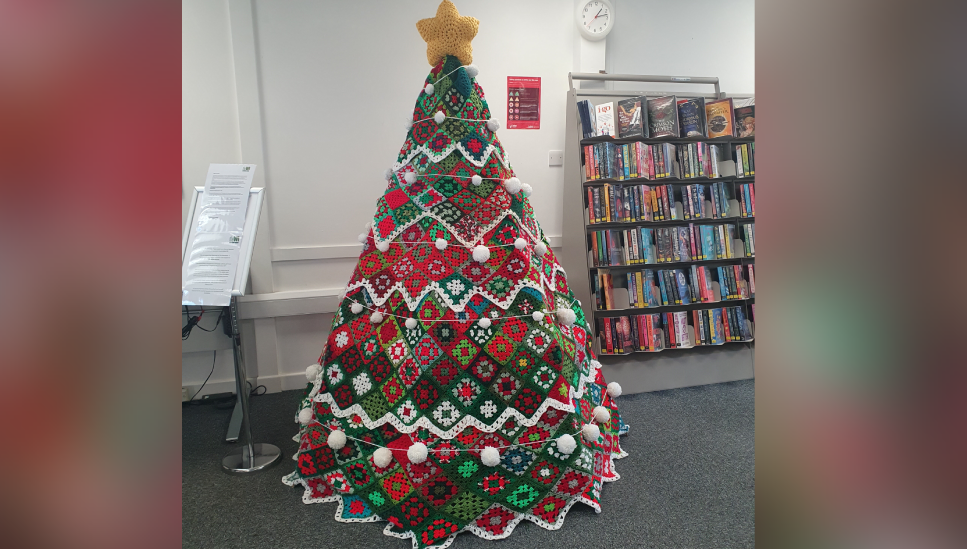 a crocheted Christmas tree standing next to a bookshelf in a library