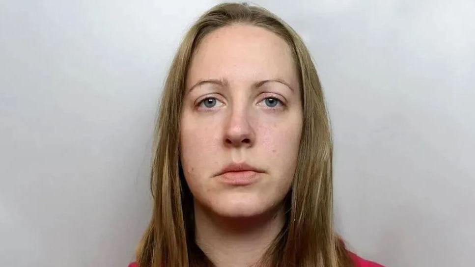 A emotionless Lucy Letby faces the camera, sporting long blond hair and wearing a red top