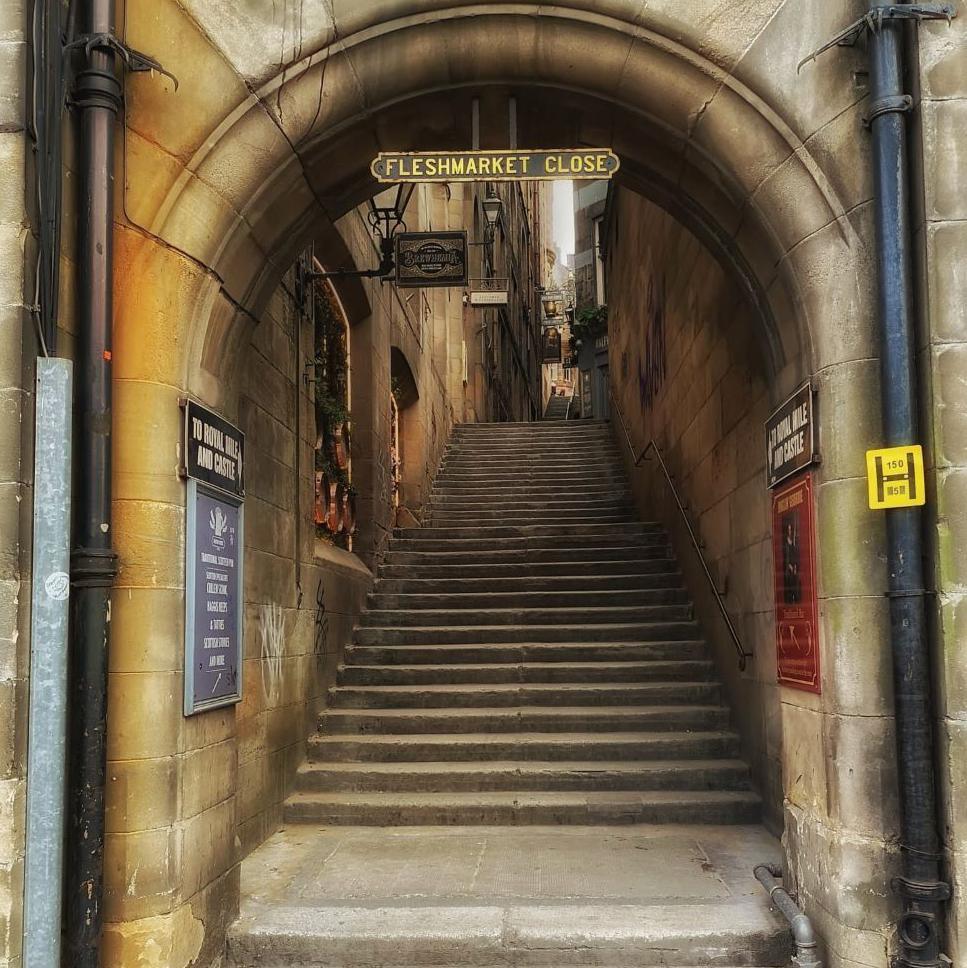 Steep steps going up into the distance. An arch way is at the start of the close and there is a little brass sign hanging from it with the name of the close.