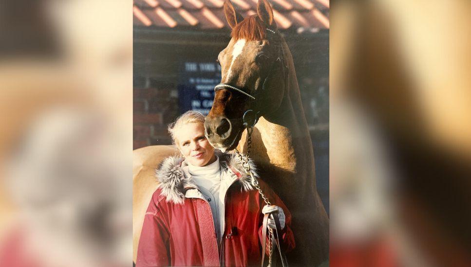 An image of Lorna Machi in a red winter coat with a brown horse stood behind her