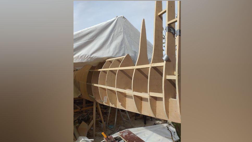 The wooden tail of the Spitfire under construction poking out of a white marquee. It is surrounded by tools, sandpaper and building materials.