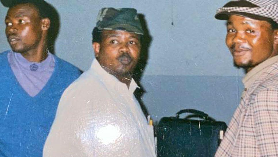 Mzolisi Dyasi, flanked by two friends, wears a white jacket and green cap as they travel to a funeral of a political activist in 1993