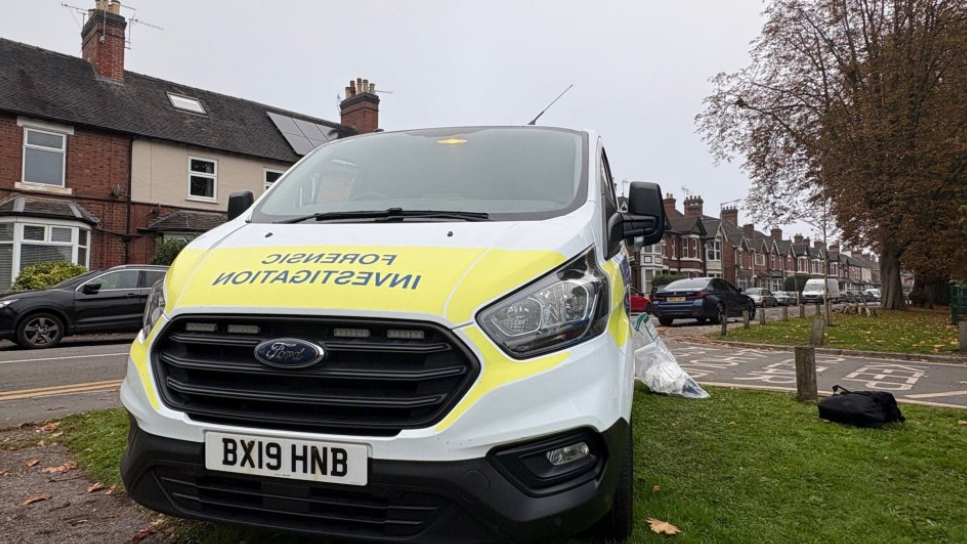 A close-up of a police van, with the words Forensic Investigation across the bonnet. There is a row of houses in the background