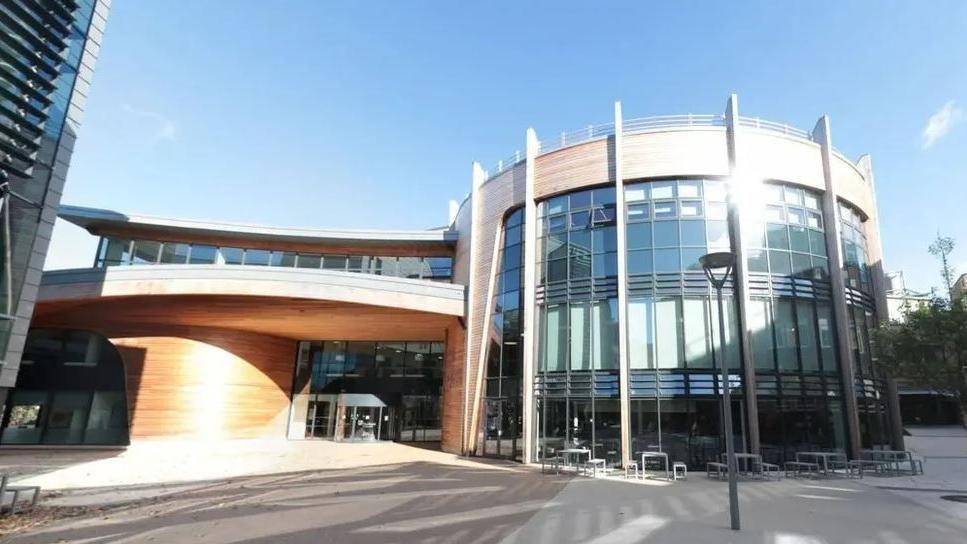 The entrance to one of Durham University's buildings. It is glass fronted with wood panelling. The section to the right is curved.