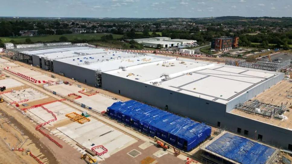 An aerial view of a data centre, made up of large white rectangular buildings, under construction