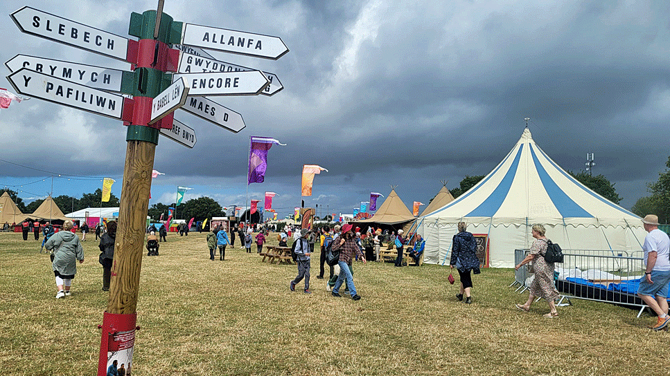 People in raincoats and others in shorts walk around the tents on the show field beneath an ominous grey sky