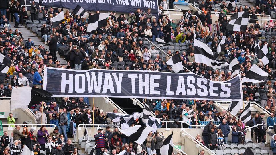 A black and white banner in a football stand reading "howay the lasses"