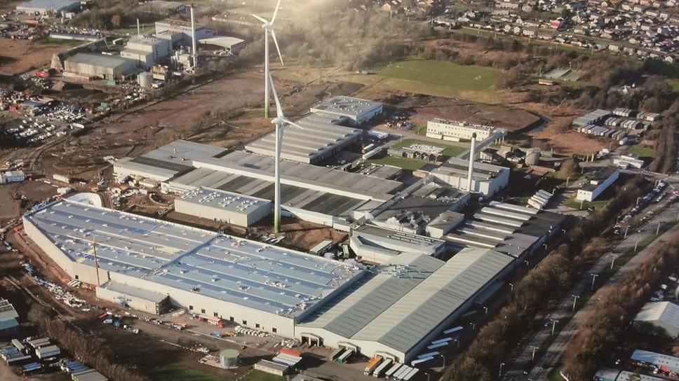 An aerial view of the former Michelin tyre factory in Dundee. Only the tops of the buildings are visible. Two wind turbines are also in the picture. The site is surrounded by a green field on one side, buildings on the left and a railway line to the right.