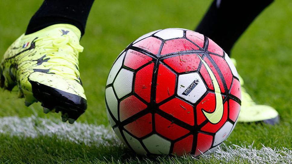 A close up of a red and white football on a grass pitch with someone in black socks and yellow football boots about to kick it