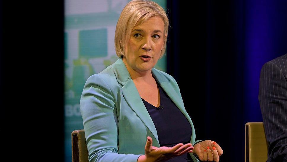Lisa Smart in a torquoise jacket and black top making a point in a TV debate
