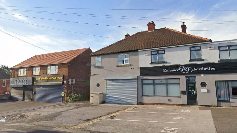 A row of shop units in a residential street. The unit in the centre has metal shutters down and is unused.