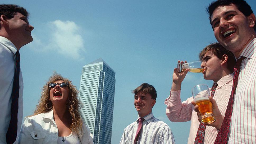 A group of nineties office workers laughing and drinking lager