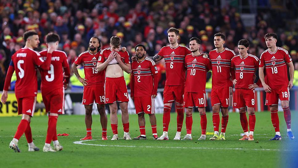 Wales players stand in a line during the penalty shootout with Neco Williams being comforted