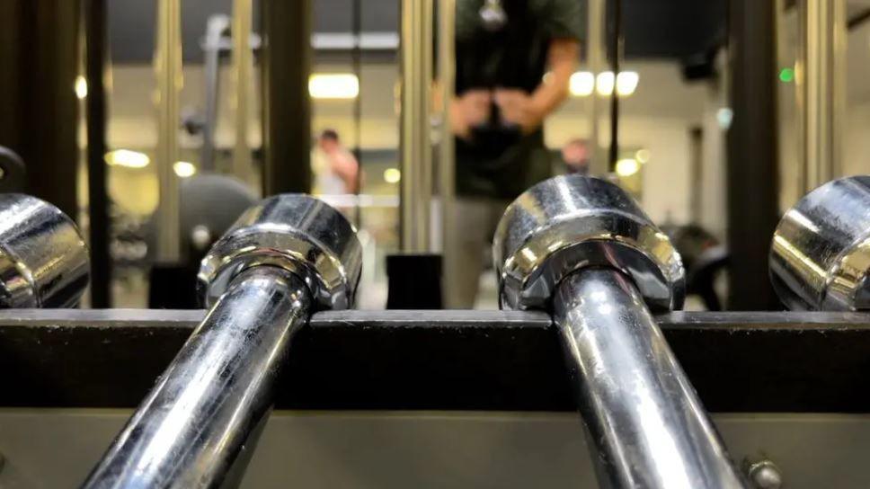 Two silver dumbbells in foreground in a rack with unidentifyable people in the background using gym equipment