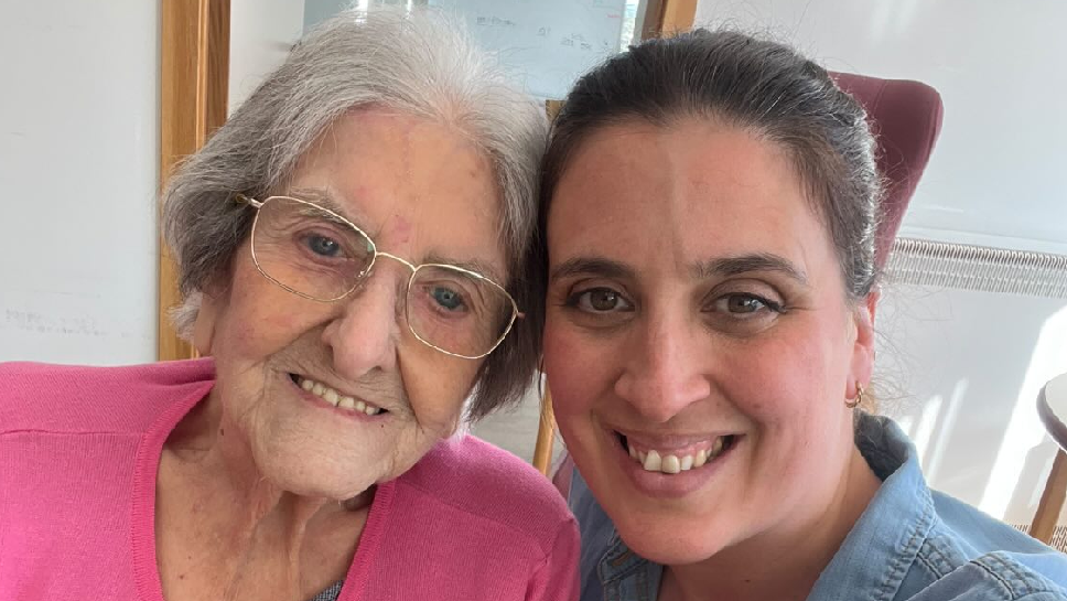 Seflie of Beca Lyne-Pirkis with her grandmother. Beca is on the right and her grandmother is on the left. Both are smiling looking at the camera. Her grandmother wears a pink top, has greying-white hair and thin-rimmed glasses. Beca has a blue top on. It is a head and shoulders shot of them.