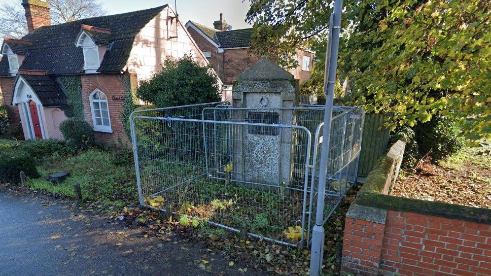 The war memorial in Shrub End in Colchester, prior to its restoration, surrounded by metal fencing