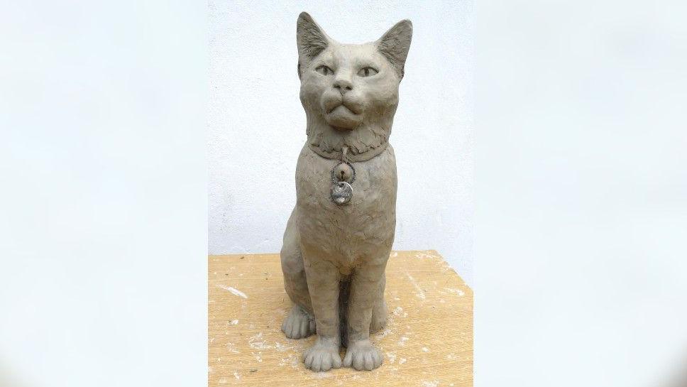 Hendrix's statue at the workshop. He is sitting with a serious look and his ears perked up. He is wearing a pendant.