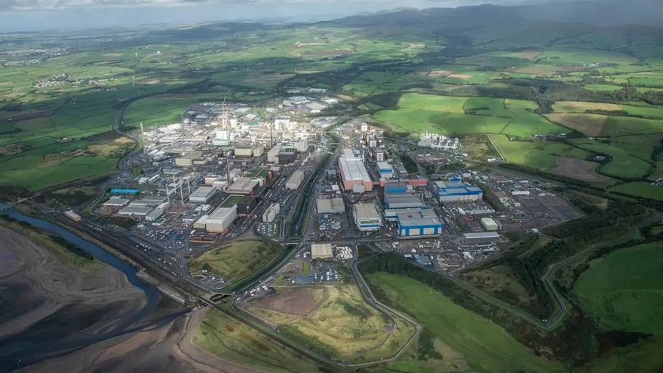 An aerial view of the Sellafield site. Dozens of concrete buildings are surrounded by green fields. In the top right, the sea can be seen.