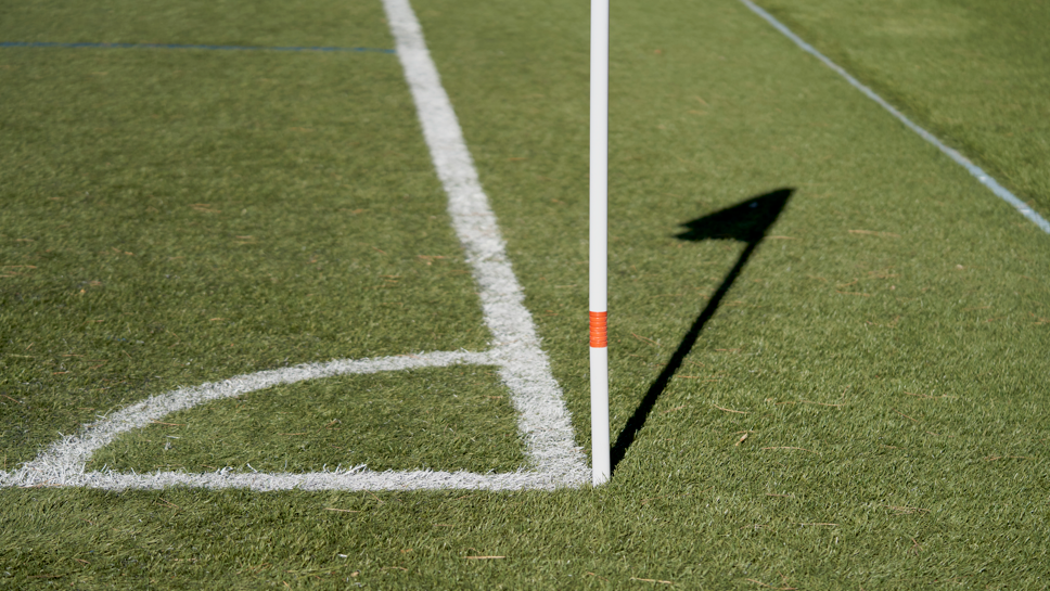 A football pitch's corner flag, with white paint on the green grass.