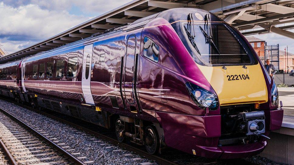 A purple and yellow high-speed train stopped at a station platform