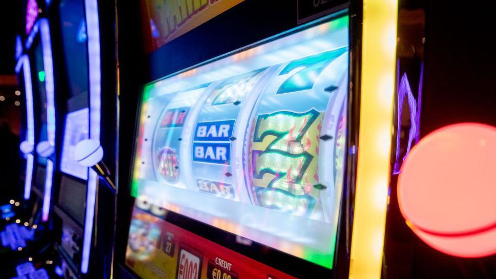 We can see the screen of a digital slot machine. It's displaying a traditional style game with three reels where we can see the number 7 and 'Bar'.