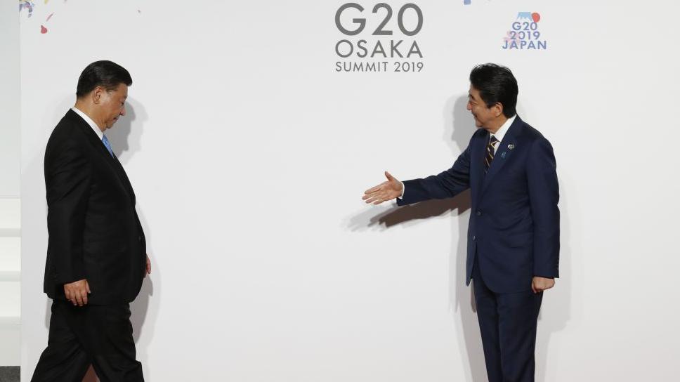 Chinese President Xi Jinping looks down as he walks toward Japanese Prime Minister Shinzo Abe, who extends his hand with a smile