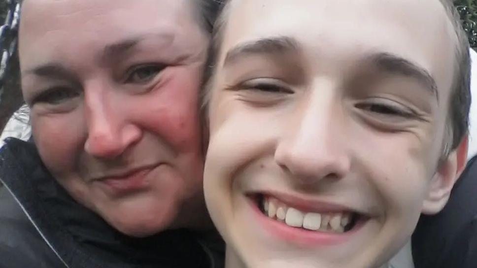 Alfie, being cuddled by his mum. Both are smiling.