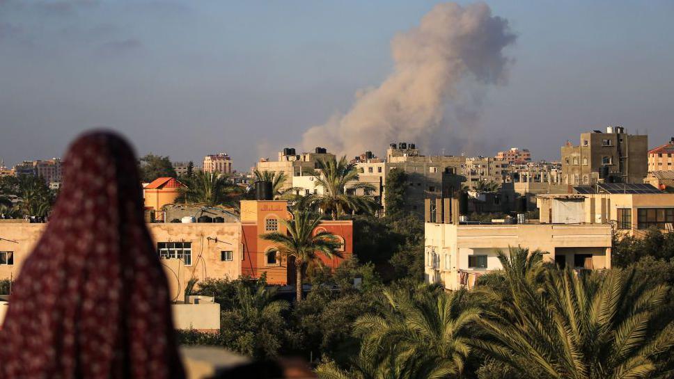 A Palestinian woman watches as smoke billows following an Israeli strike south of Gaza City, in the town of al-Zawaida, in the central Gaza Strip (11 June 2024)