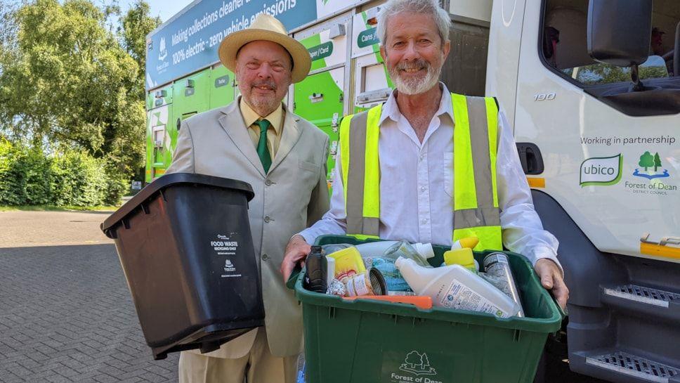 Two men holding waste bins standing in front of a new electric lorry