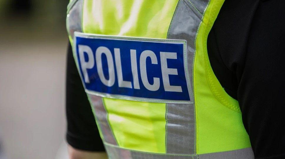 Stock photo of police officer's high visibility vest. The vest is green with grey stripes and the word "police" in white letters on a blue background, in a rectangle in the middle of the back of the vest.