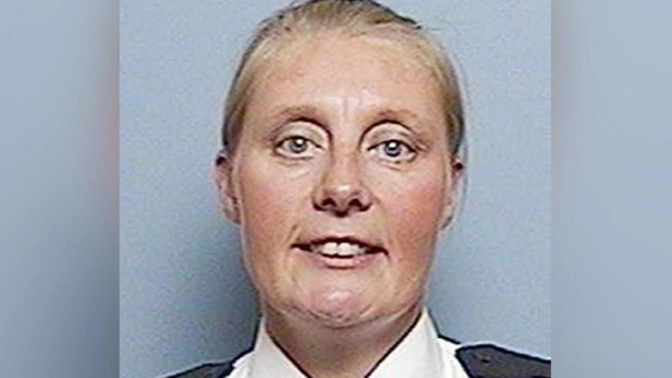 Sharon Beshenivsky smiling at the camera with her blonde hair tied back in a ponytail. She is wearing her police uniform and is stood in front of a grey background. 