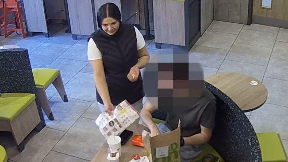 Nirix Stanescu uses a piece of paper to cover a phone on a table. There is a man sat down.