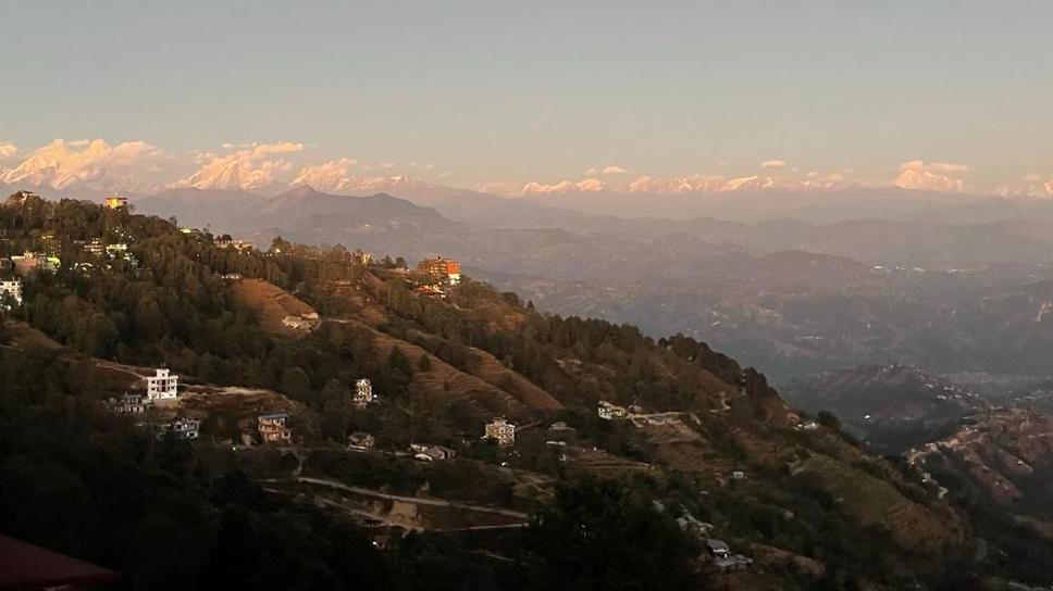 View of a hill in the foreground with Himalaya mountains and some peaks visible in the background