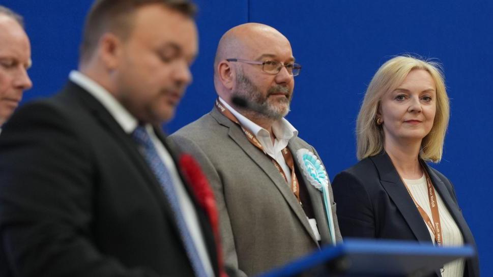 Liz Truss stands on the podium at Alive Lynnsport in King's Lynn, Norfolk, during the count in the 2024 General Election