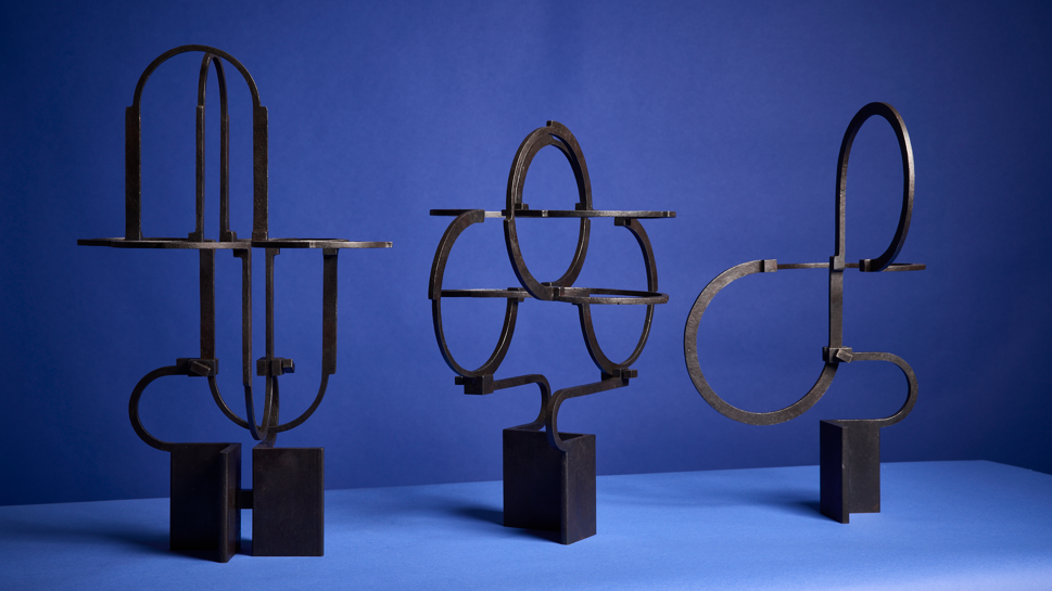 Three of Mr Pearson's sculptures pictured on a blue table. The sculptures are made from metal and are mounted on plinths.