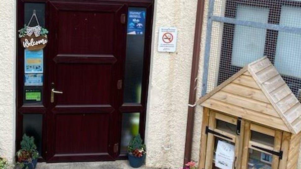 Markham playgroup entrance, a brown door is visible to the left and a wooden animal hutch with items like postcards is to the right. 