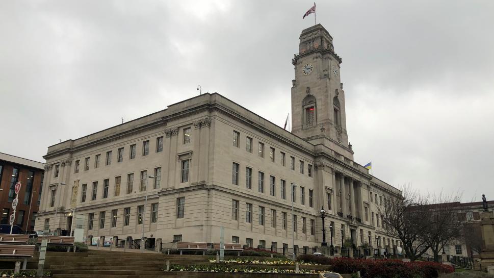 A cream-coloured town hall building surrounded by gardens.