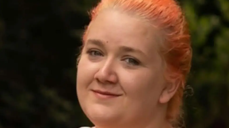 Ms Whyte is smiling at the camera in a close-up photo. She has dyed red hair puled back.
