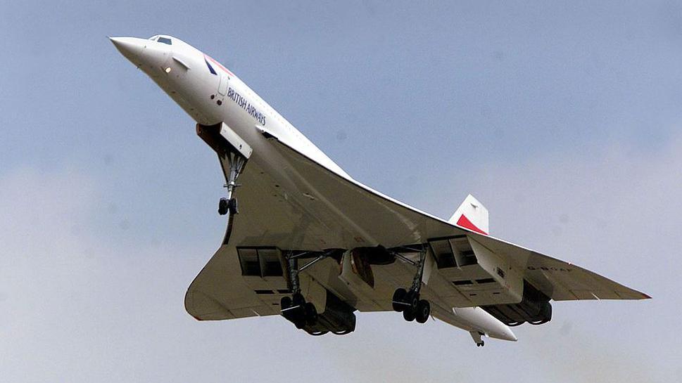 A British Airways Concorde takes off from Heathrow Airport in London. The landing gear can be seen retracting under the aircraft's distinctive v-shaped wings, A splash of red can be seen on the tail.