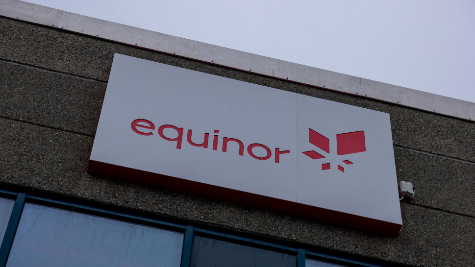 A sign for the Norwegian state oil company Equinor. The sign, on top of a dark-coloured building, is white, with the company name in red text, next to its logo, which is also in red.